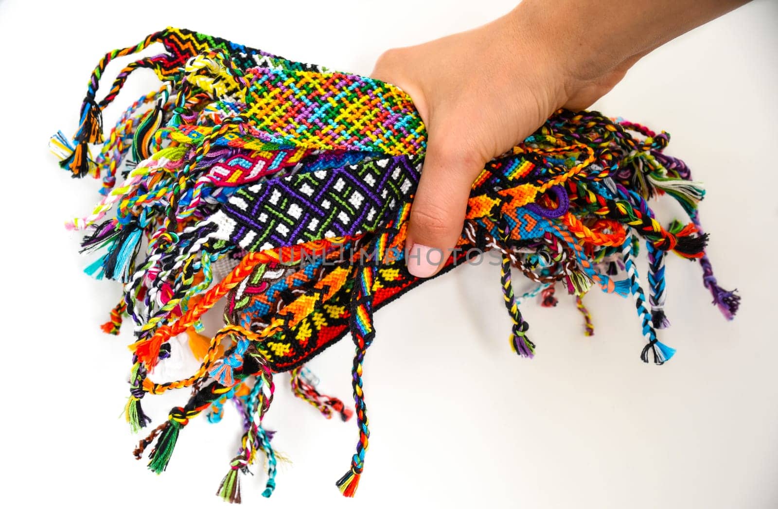 Female hand holding many woven multi-colored DIY friendship bracelets handmade of embroidery thread with knots on white background.