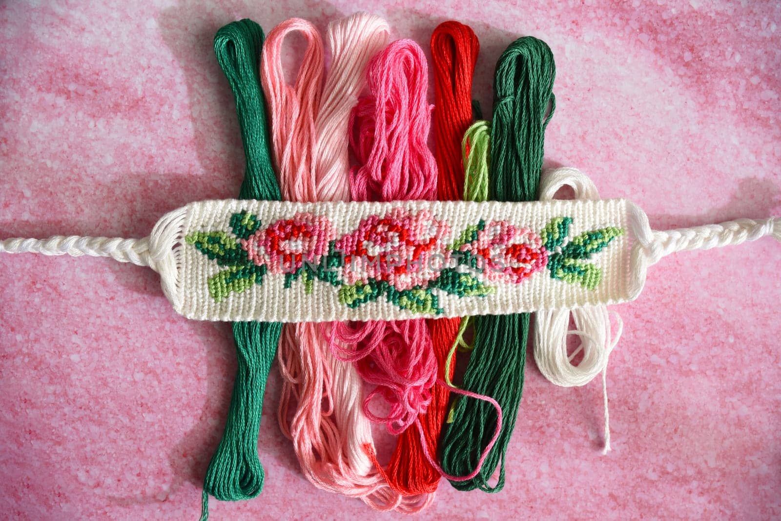 Woven DIY friendship bracelet with bright flower pattern Rose near scissors and skeins of embroidery thread