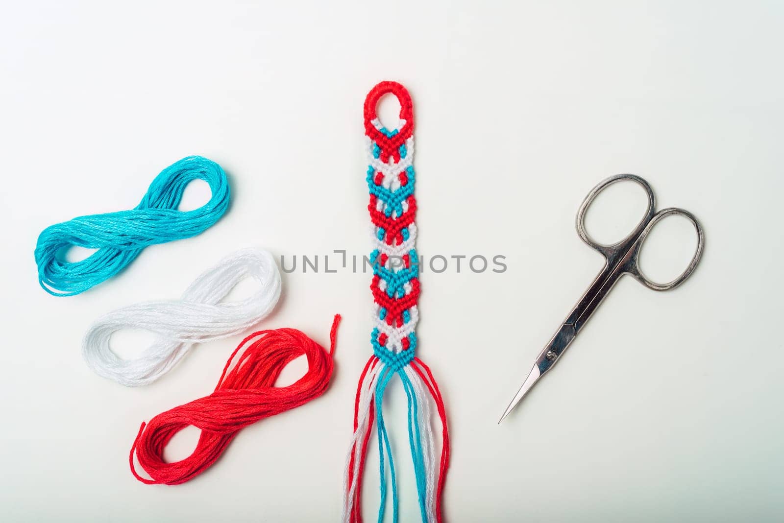 Unfinished woven DIY friendship bracelet with boho pattern next to scissors on white background