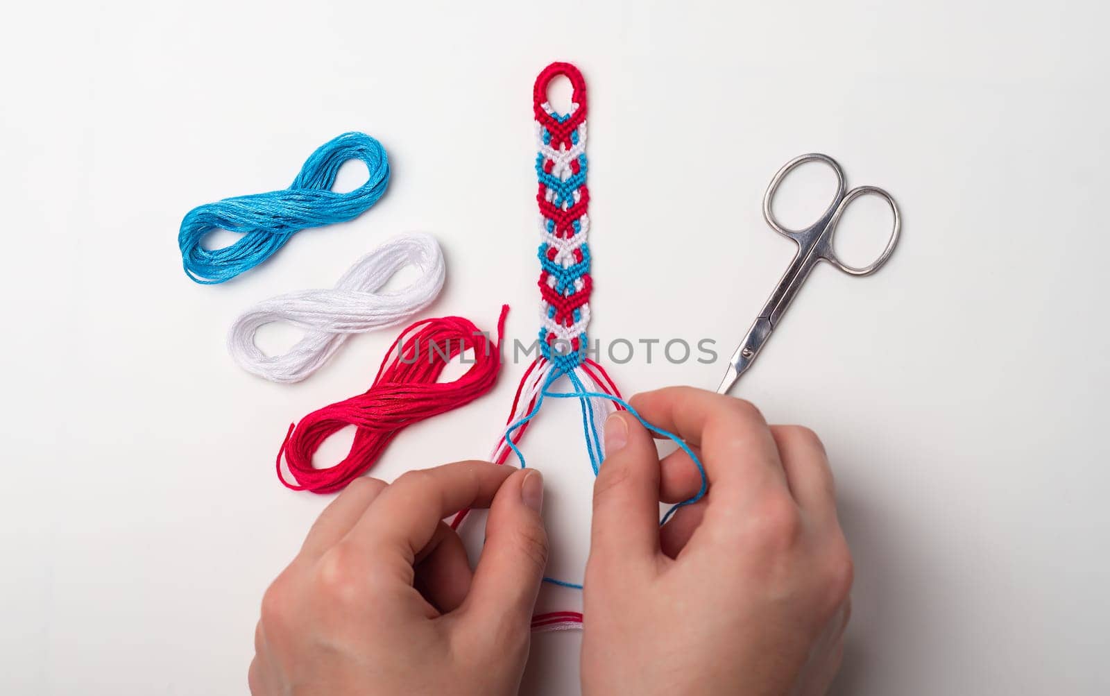 Process of weaving knot for DIY friendship bracelet. Female hands. step by step. White background with copy space, scissors and thread