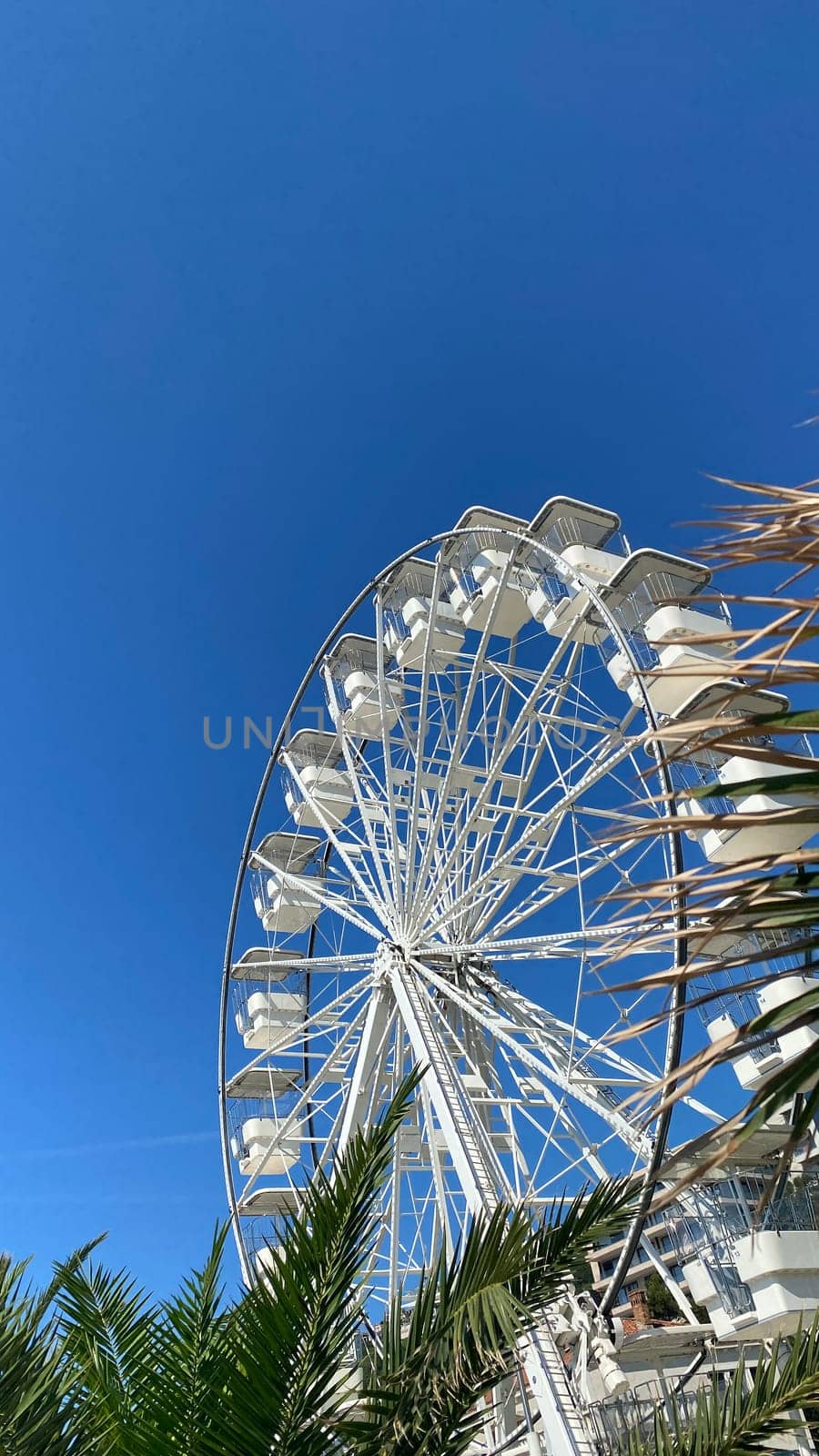White Ferris wheel against bright blue sky, seen from below