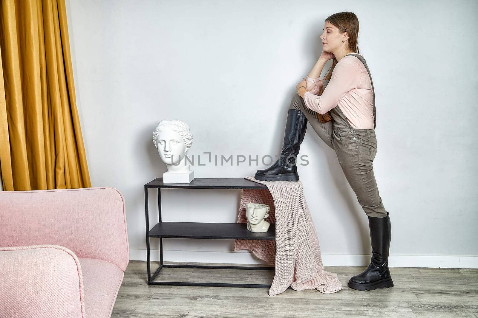 Fashionable model strikes a pose in trendy boots, highlighting her outfit in a chic room with modern decor.