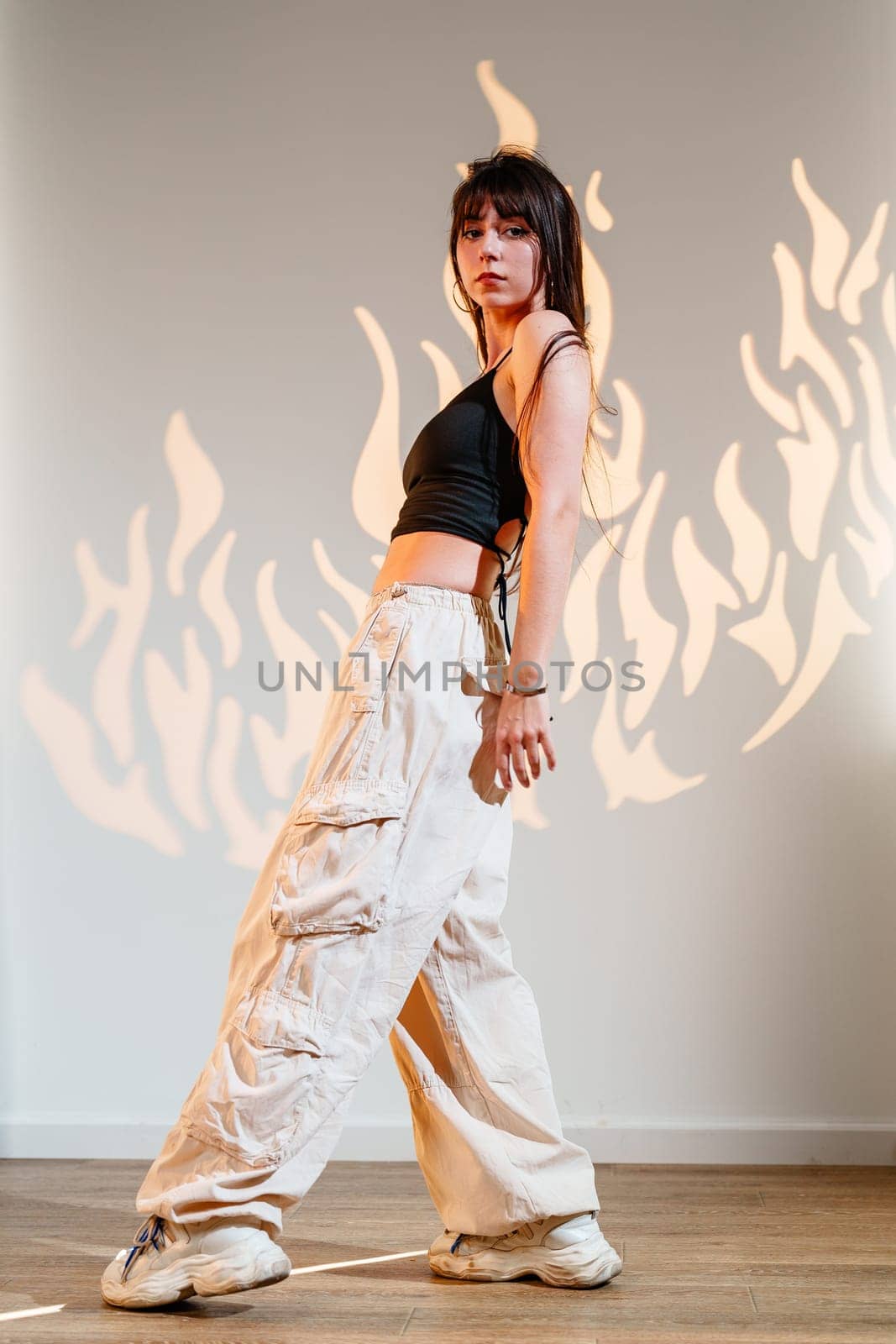 A skilled dancer displays fluid movements in a spacious studio, wearing casual attire. The backdrop features artistic flame designs, enhancing the energetic atmosphere.