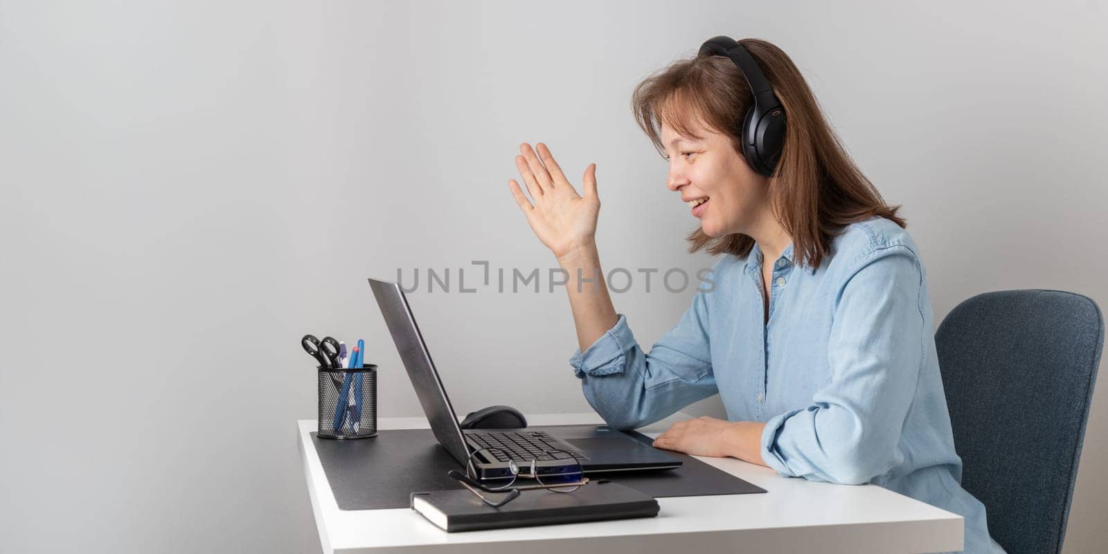 Cheerful freelance professional woman wearing big headphones talking on online chat meeting using laptop, speaking on video conference call, smiling, enjoying work online communication