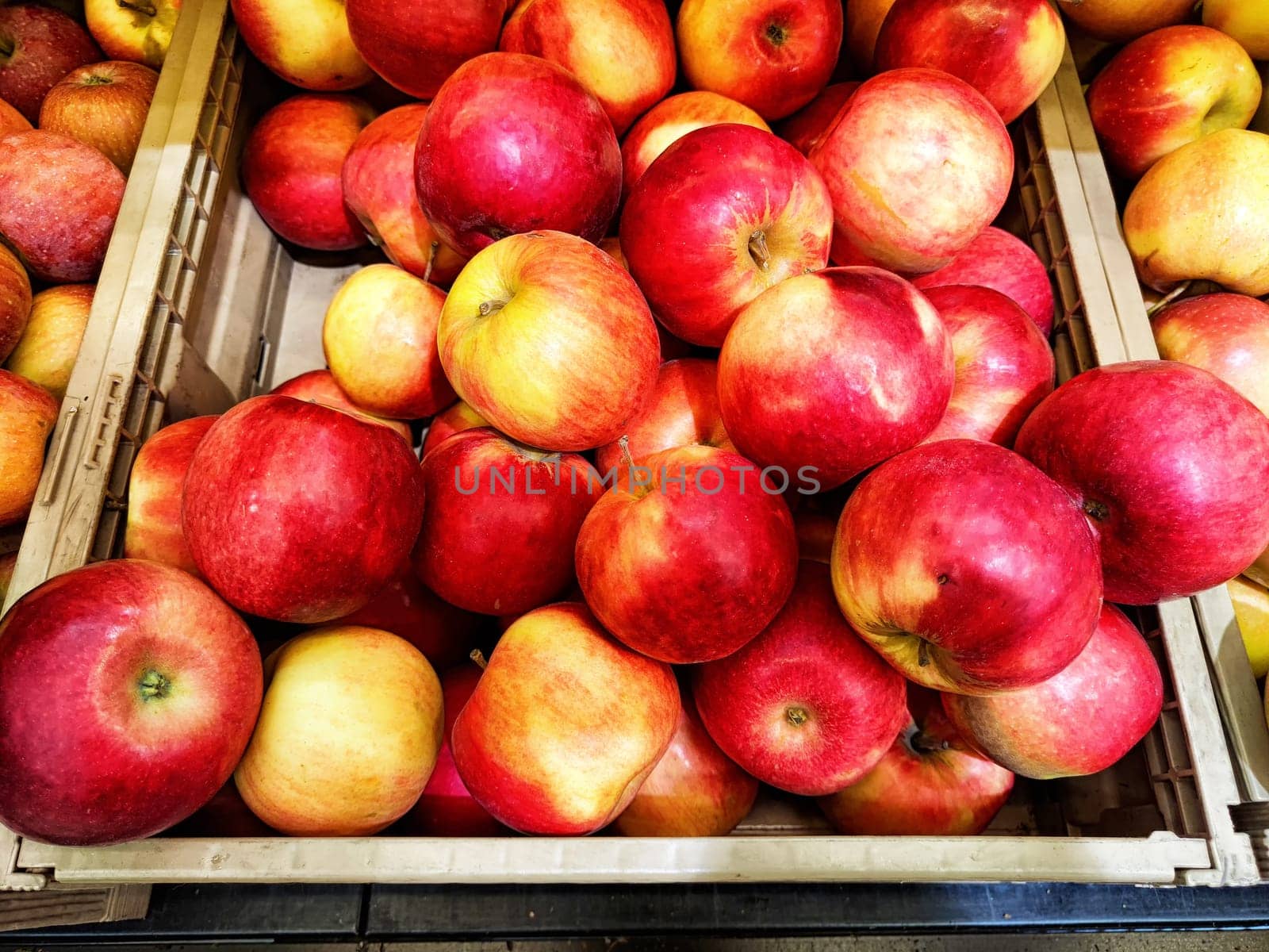 Vibrant red apples fill a wooden crate at a lively market, showcasing the harvest's seasonal bounty in fall.
