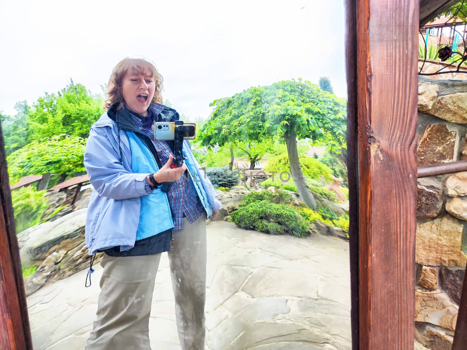 Blonde woman enjoying a fun moment by taking a silly selfie in a curved mirror at a park during her outdoor adventure.