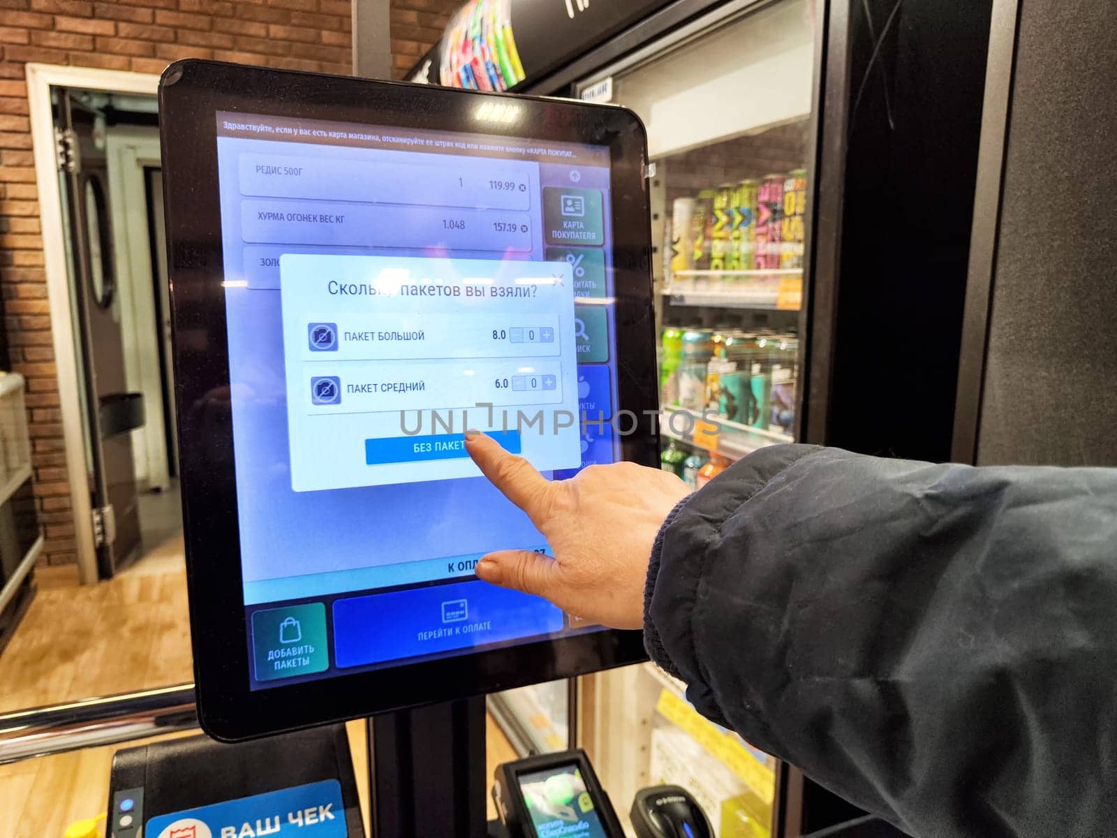 Kirov, Russia - December 03, 2024: Shoppers use a touchscreen to weigh products and manage payments at a self-service checkout station in a retail environment.