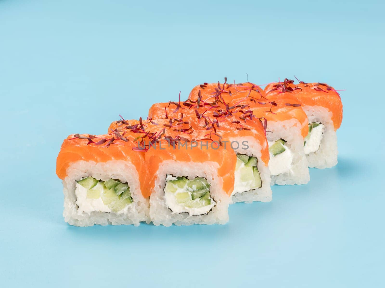Studio photography of Philadelphia Roll of velvety cream cheese and cucumber wrapped in perfect seasoned sushi rice and fresh salmon, decorated microgreens. Isolated on solid light blue background