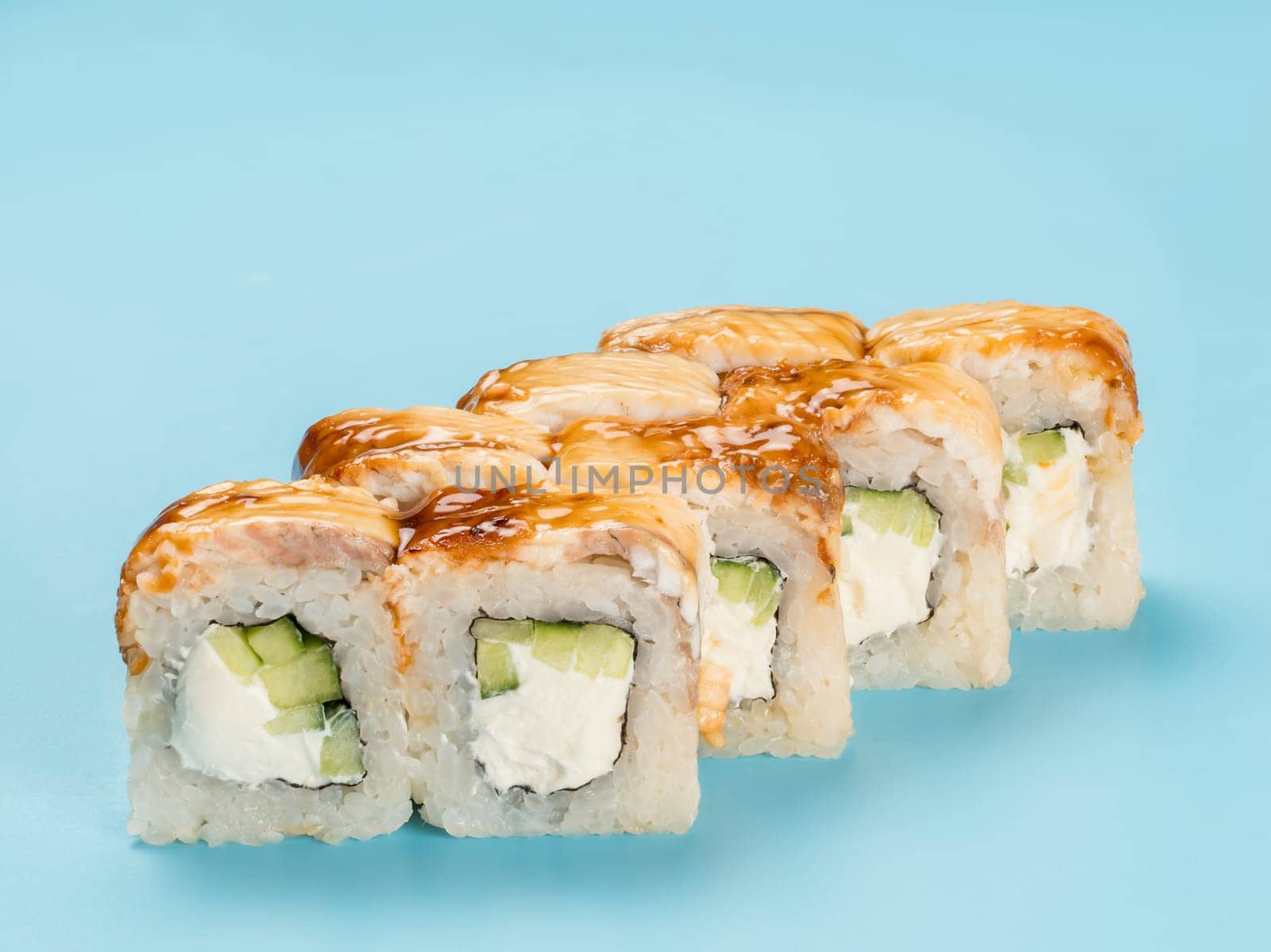 Studio photography of Philadelphia Roll of velvety cream cheese and cucumber wrapped in perfect seasoned sushi rice and fresh unagi smoked eel. Isolated on solid light blue background
