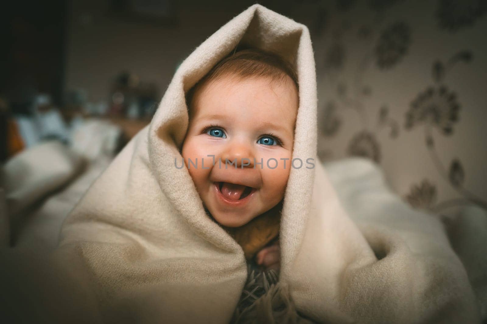 Smiling baby girl crawling on bed under the blanket. Adorable kid portrait. 5 month old child. Childhood concept. High quality photo