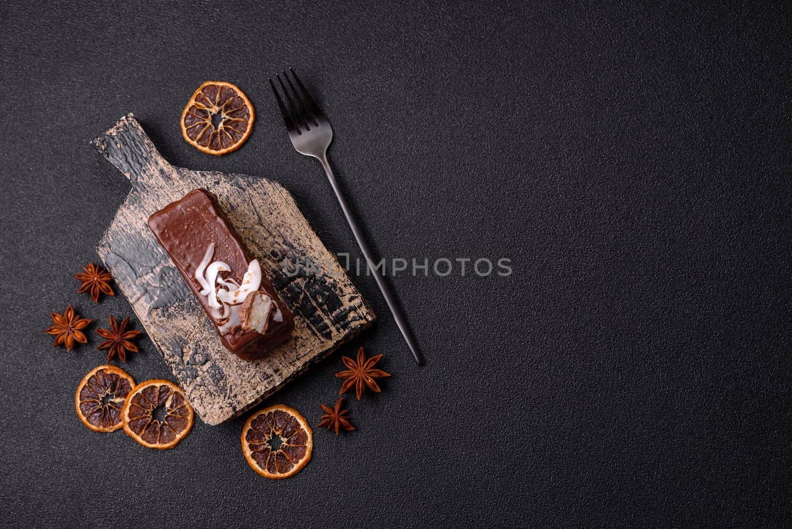 Piece of sweet chocolate bounty cake with coconut flakes and sponge cake on dark concrete background