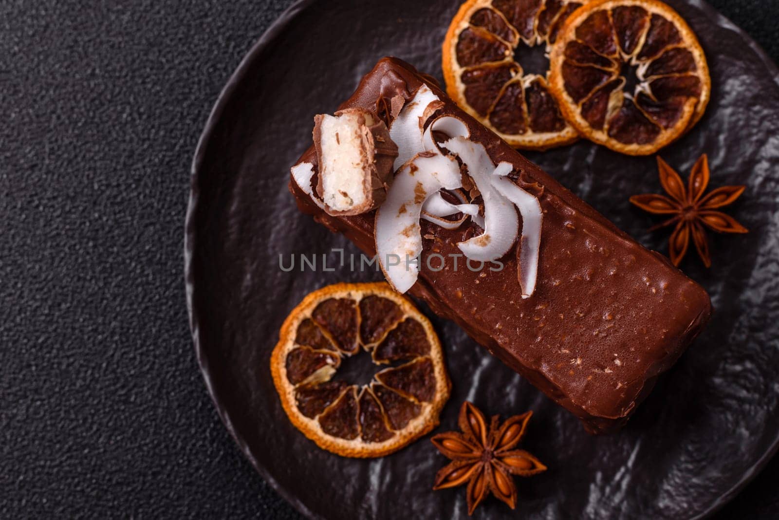 Piece of sweet chocolate bounty cake with coconut flakes and sponge cake on dark concrete background