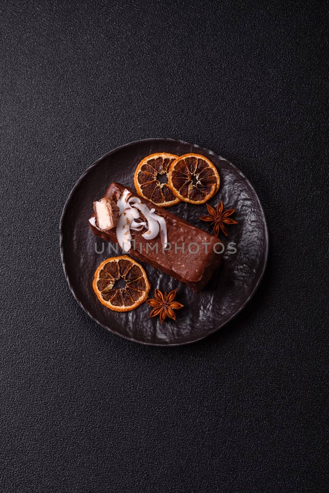 Piece of sweet chocolate bounty cake with coconut flakes and sponge cake on dark concrete background