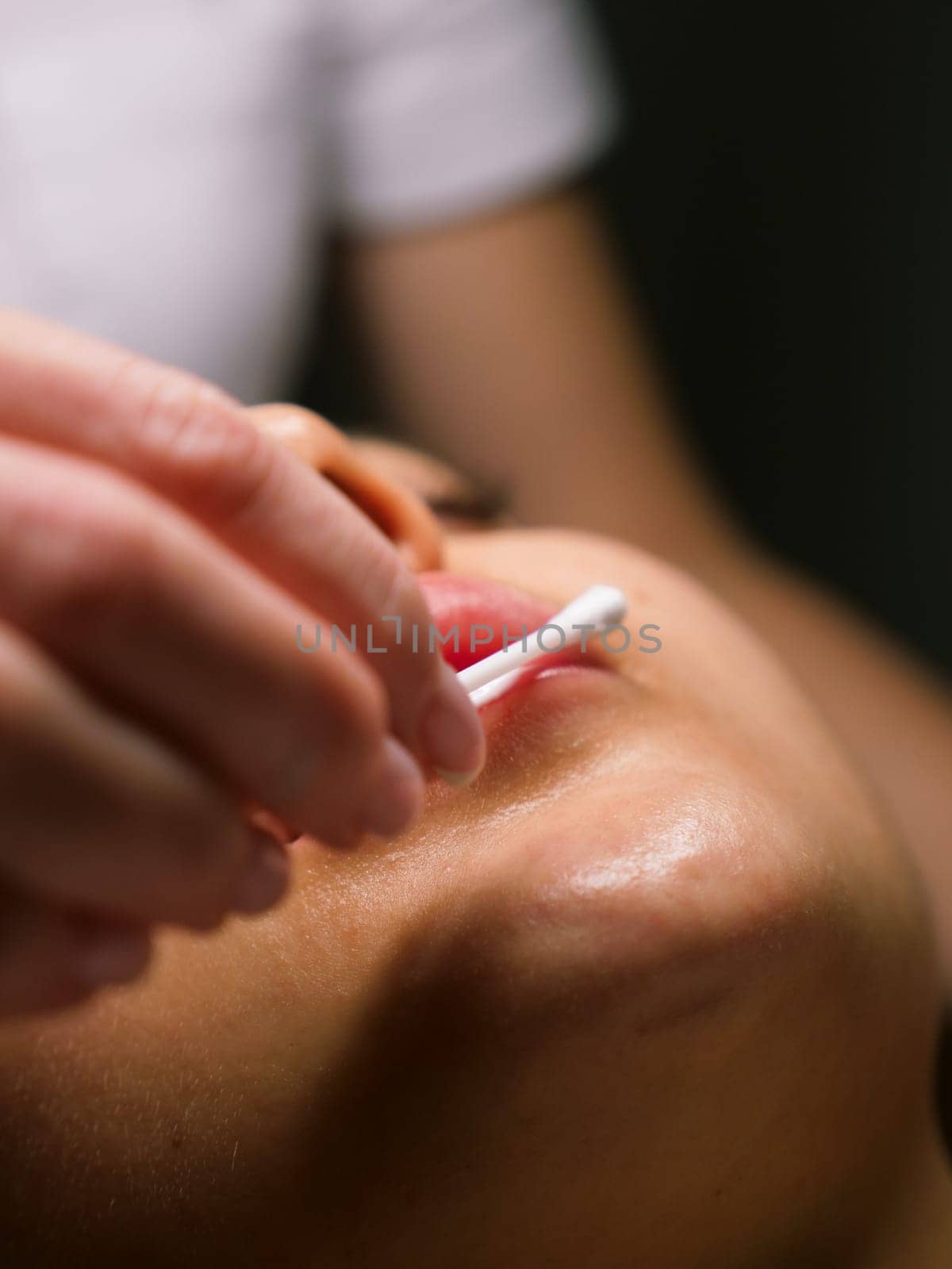 Moisturizing and nourishing lips in a beauty salon for a young Caucasian woman, close-up, vertical, stories