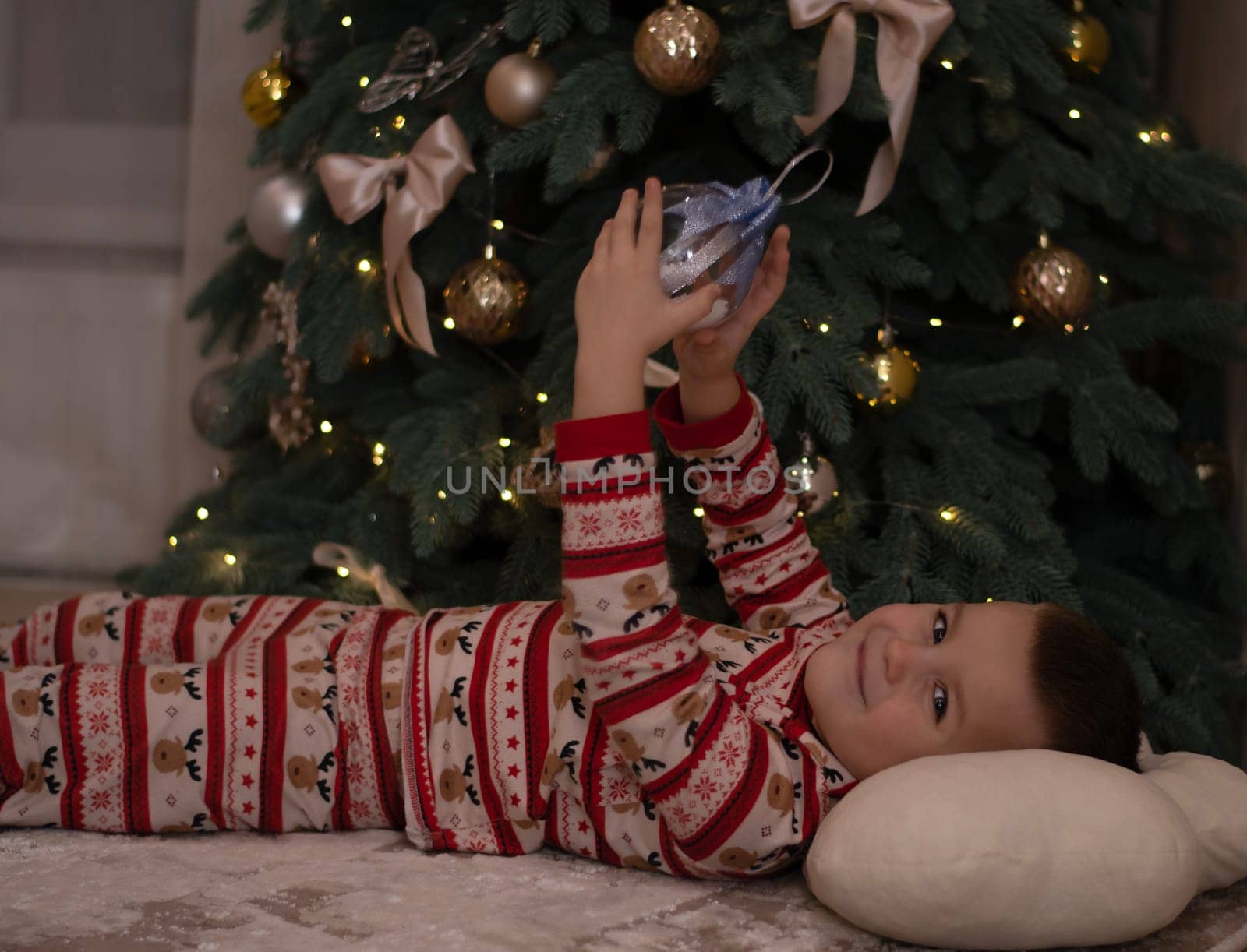Christmas. A 5-year-old boy in New Year's pajamas lies on the floor near the Christmas tree and looks at the New Year's ball. festive atmosphere