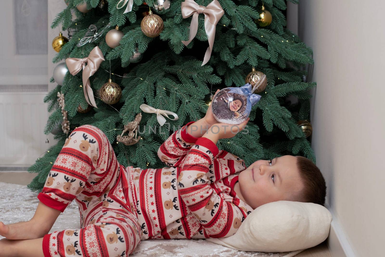 Christmas. A 5-year-old boy in New Year's pajamas lies on the floor near the Christmas tree and looks at the New Year's ball. festive atmosphere