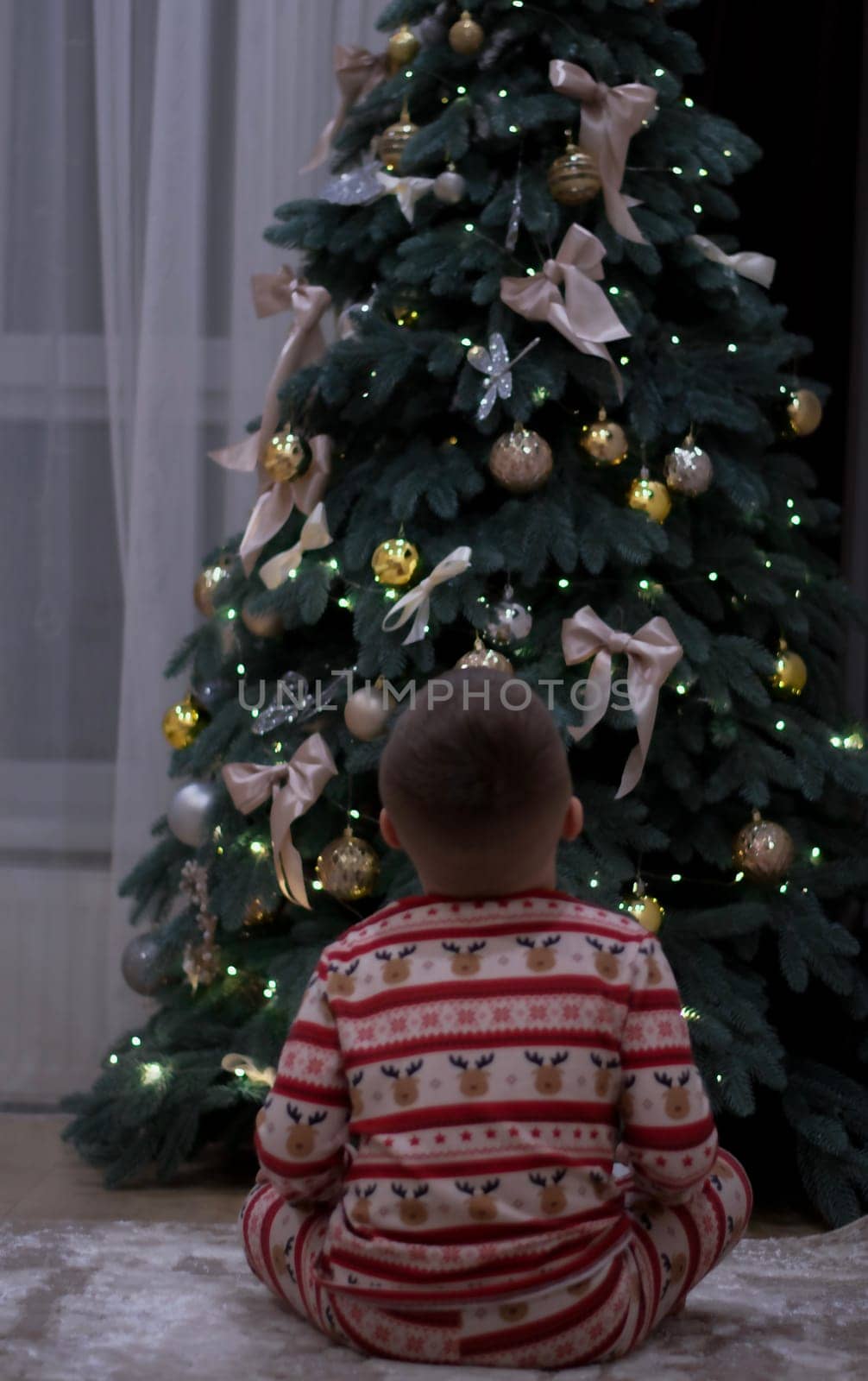 Christmas, a boy in New Year's pajamas sits on the floor and works on the Christmas tree. Rear view, without face
