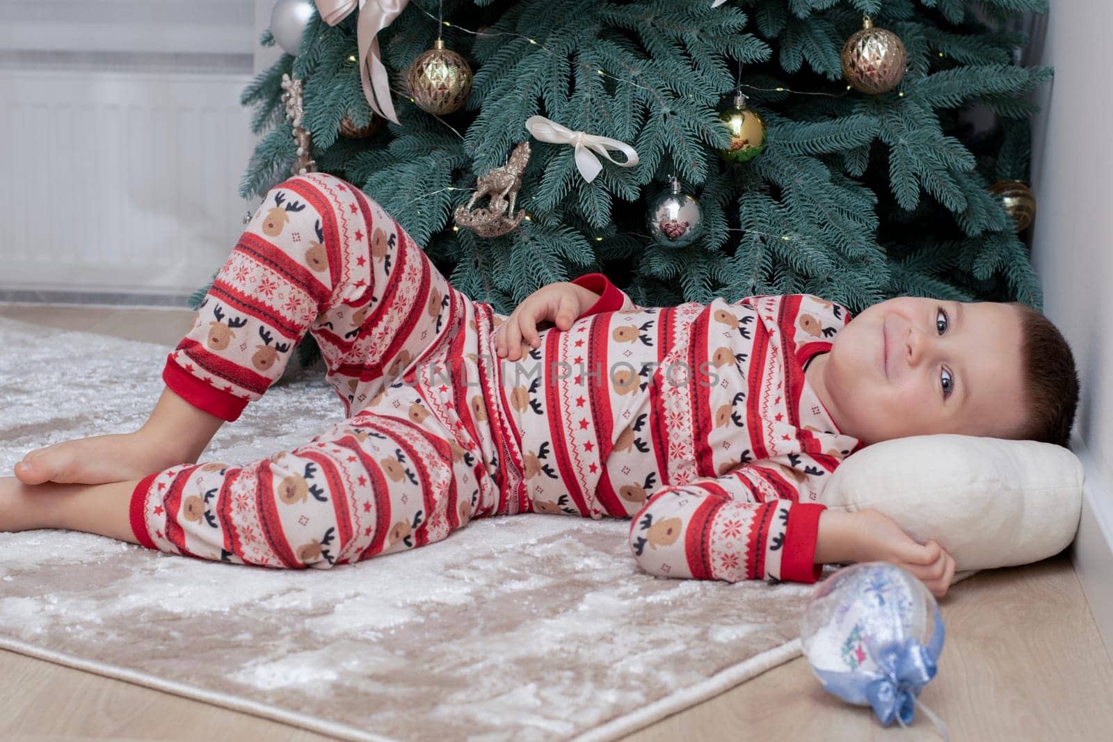 Christmas. A 5-year-old boy in New Year's pajamas lies on the floor near the Christmas tree and looks at the New Year's ball. festive atmosphere