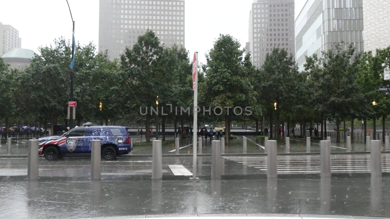 New York City, United States - 10 Sept 2023: Manhattan Downtown Financial District. People with umbrella on rainy day. World Trade Center Oculus, memorial 911 Museum, Police car on Greenwich street.