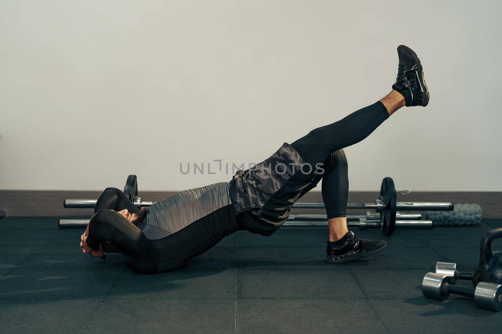 A person exercises on a gym mat, lifting one leg upward while keeping the other bent. This movement emphasizes core strength and is performed in a modern gym setting.