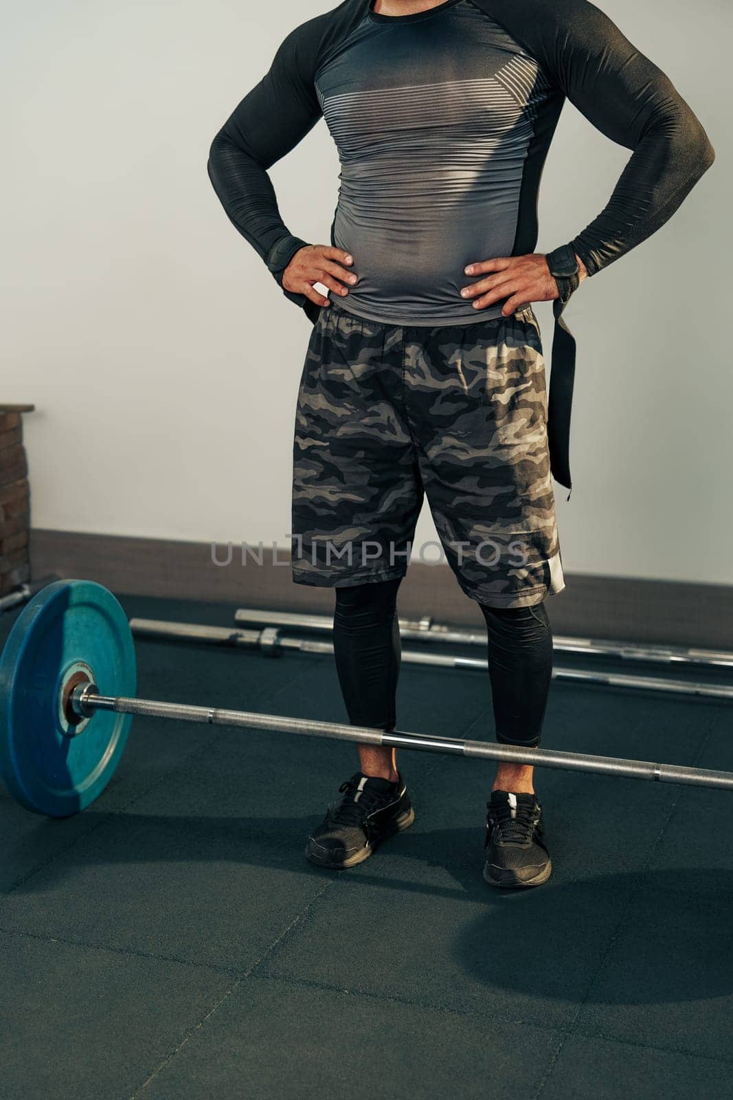 A determined fitness enthusiast stands confidently in a gym, prepared to lift a barbell loaded with weights. The athlete wears fitted workout attire, showcasing dedication to fitness.