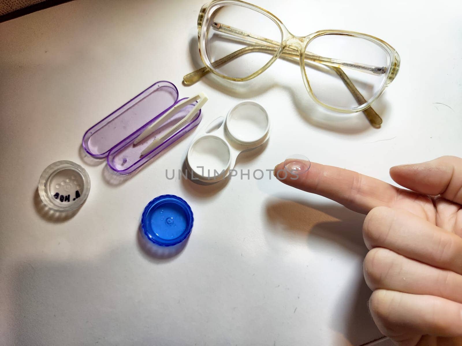 A person prepares to place a contact lens on their finger while organized eyewear tools and solutions are neatly arranged nearby.