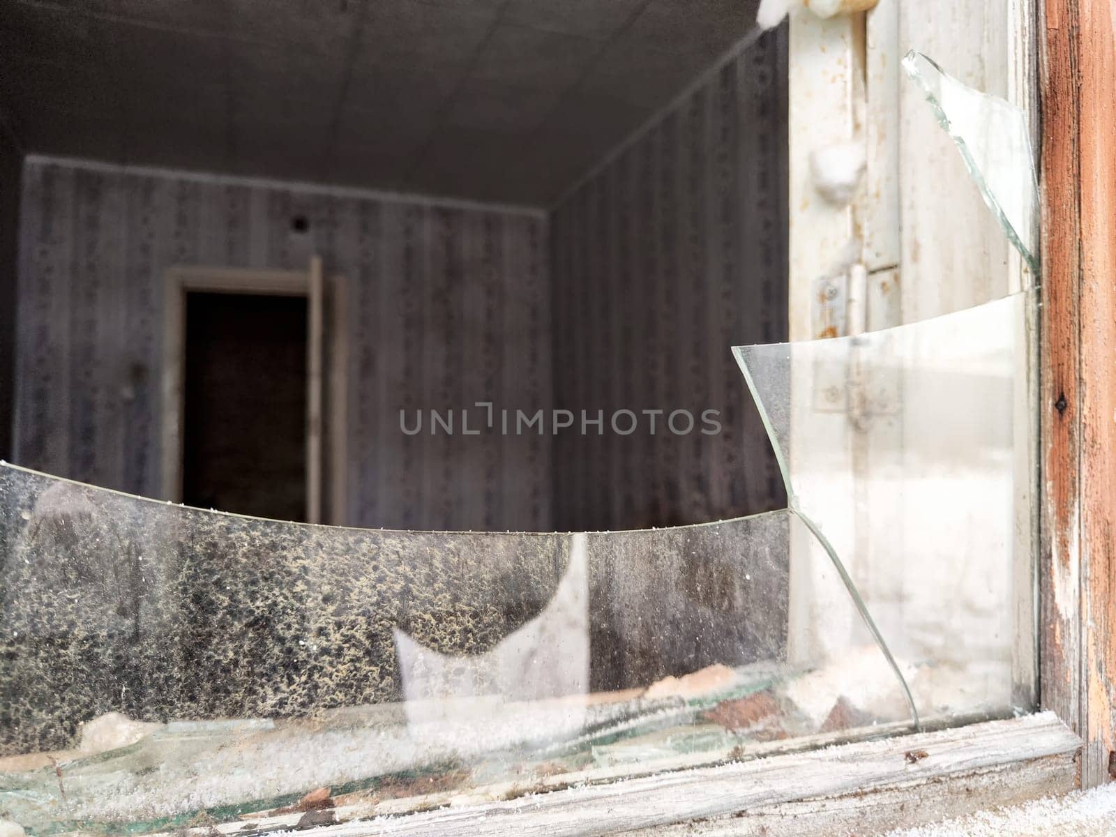 Shattered glass in a broken window showcases a neglected interior, suggesting abandonment and decay in a forlorn location.