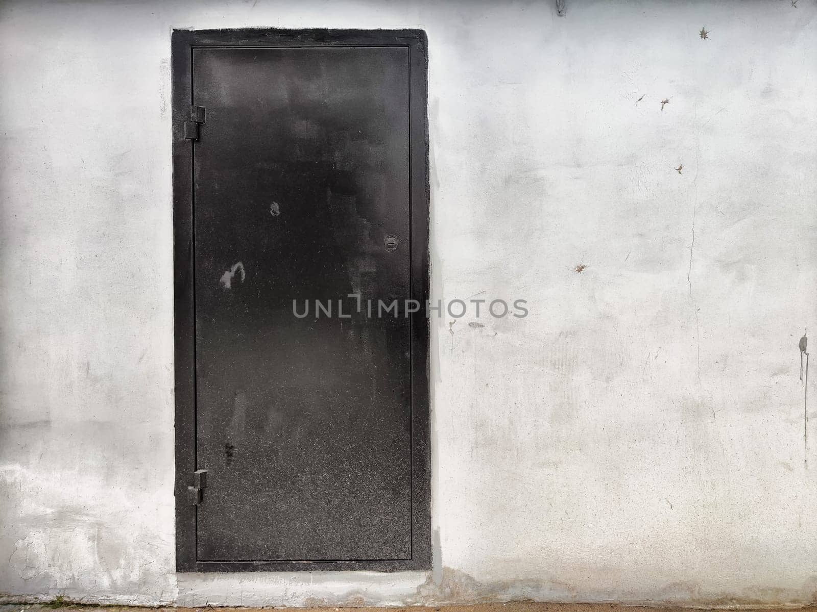 A black door stands prominently against a weathered gray wall, highlighting urban elements in broad daylight.