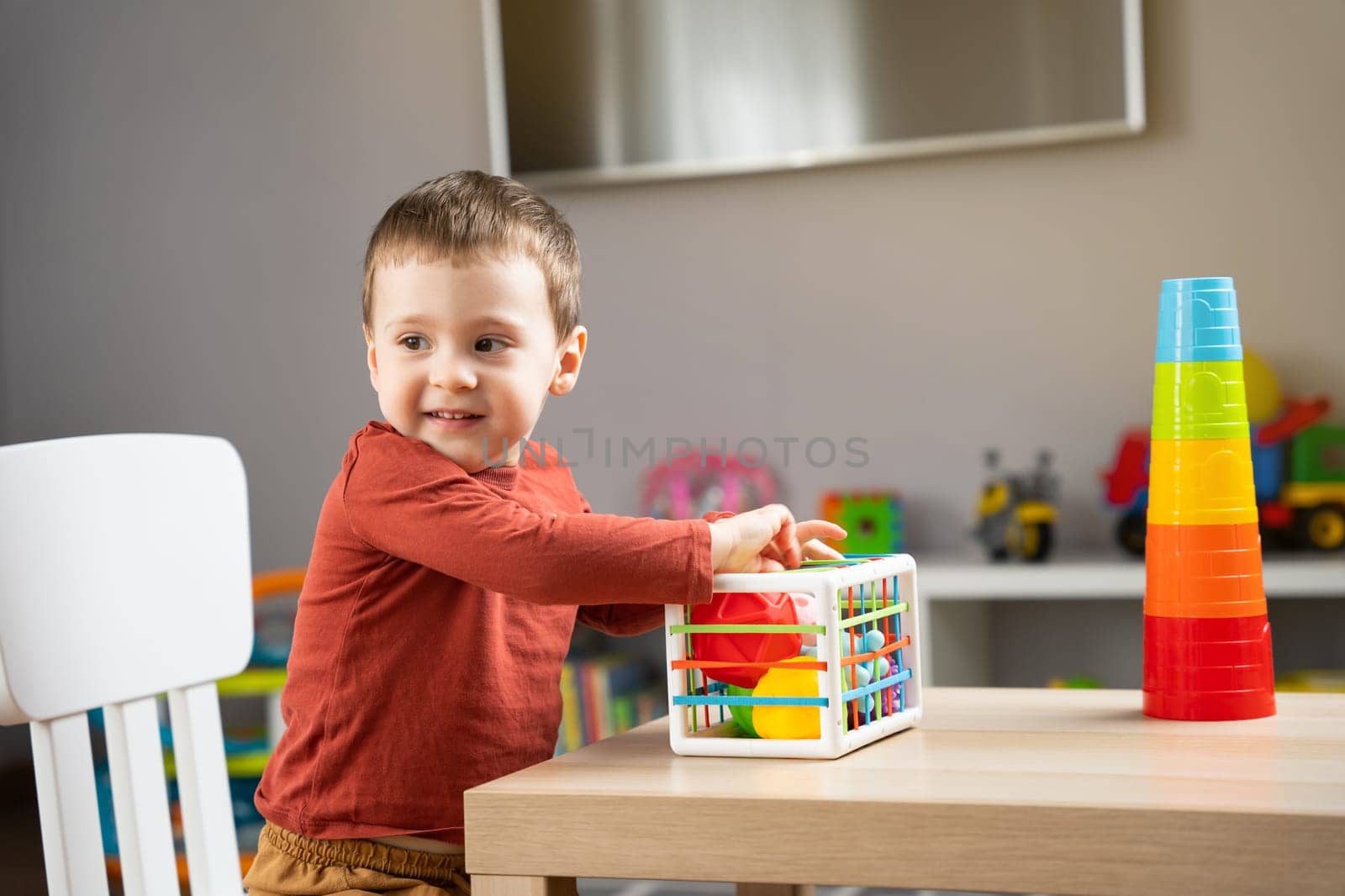 A cute little toddler boy of two years old plays with multi-colored balls and sits at a children's table in his room. Tactile sensory balls. Educational toys for children. Soft selective focus