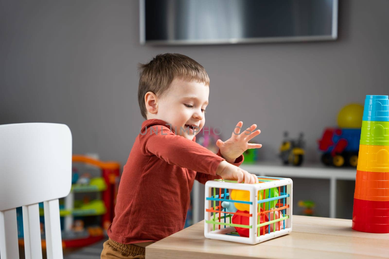 A cute little toddler boy of two years old plays with multi-colored balls and sits at a children's table in his room. Tactile sensory balls. Educational toys for children. Soft selective focus