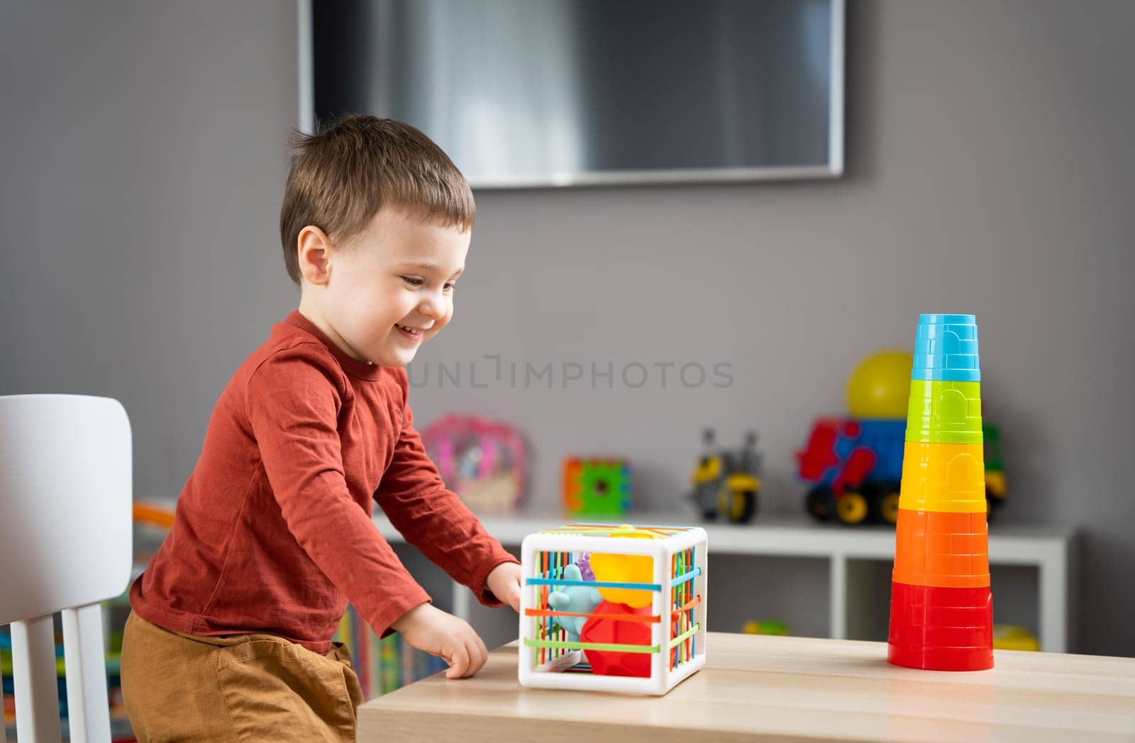 A cute little toddler boy of two years old plays with multi-colored balls and sits at a children's table in his room. Tactile sensory balls. Educational toys for children. Soft selective focus