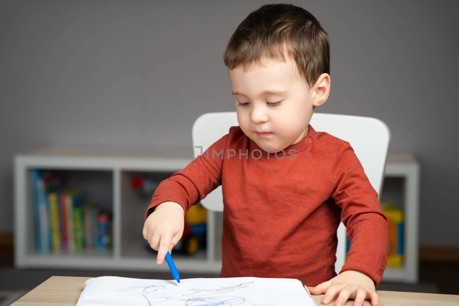 A cute attentive little toddler boy of two years old draws with markers in the album in the children's room at home. Educational activities for kids
