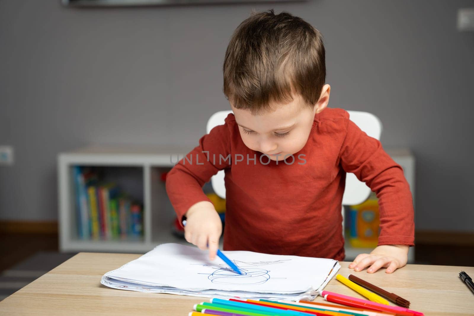 A cute little toddler boy of two years old draws with markers in the album in the children's room at home. Educational activities for kids