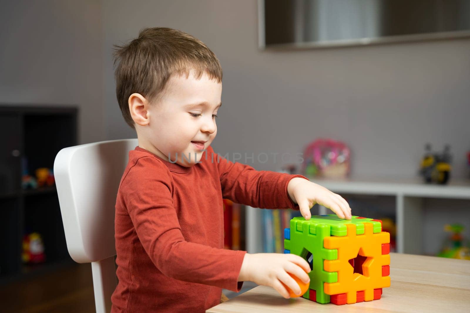 A cute happy little toddler boy of two years old sits at a children's table and plays with multi-colored sorter. Educational logic toys for children. Soft selective focus