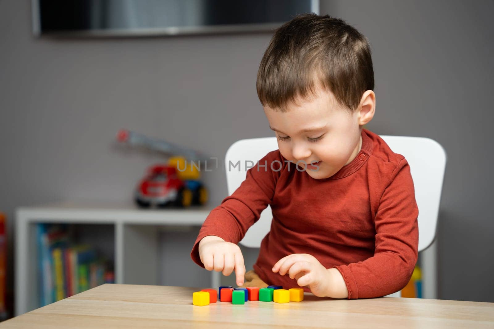 A happy cute little toddler boy of two years old sits at a children's table and plays with colorful cubes. Educational logic toys for children. Soft selective focus