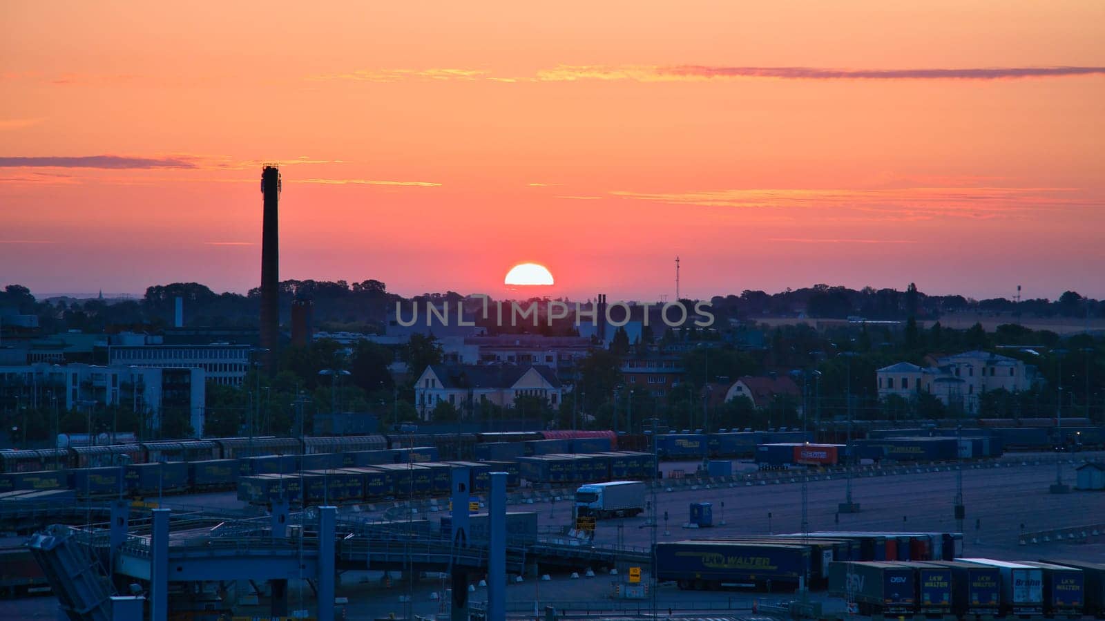 The harbor of Trelleborg, Sweden, at sunrise with calm water, blue harbor facilities and a city view in the background.
