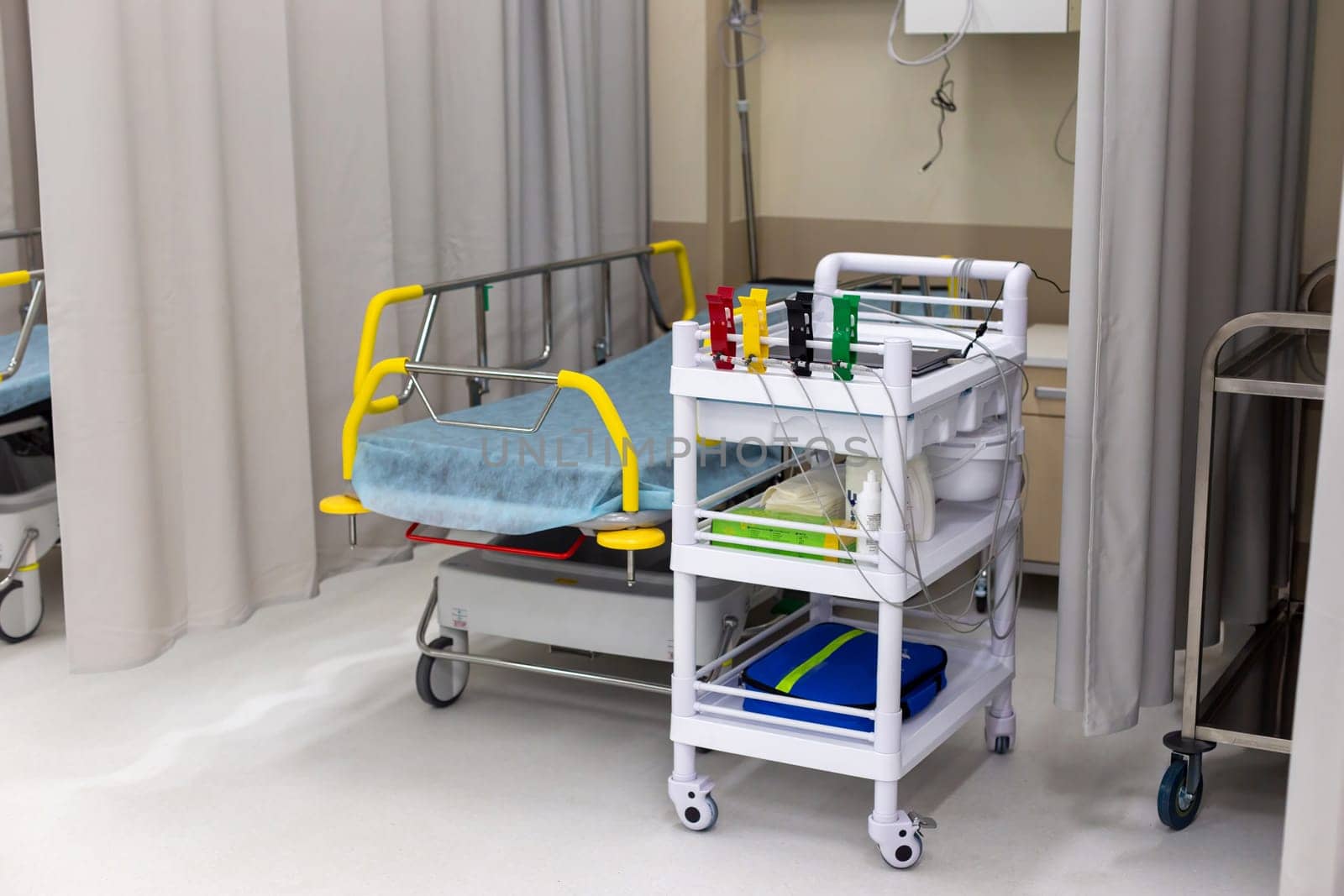 Modern hospital room, in the emergency department, equipped with a bed for the patient and a medical trolley with supplies