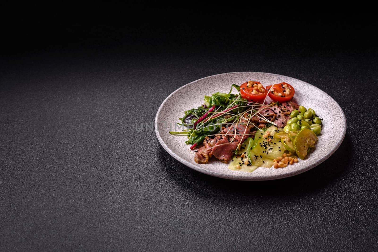 Warm salad consisting of slices of roast beef, greens, tomatoes, cucumbers, green beans on a dark concrete background