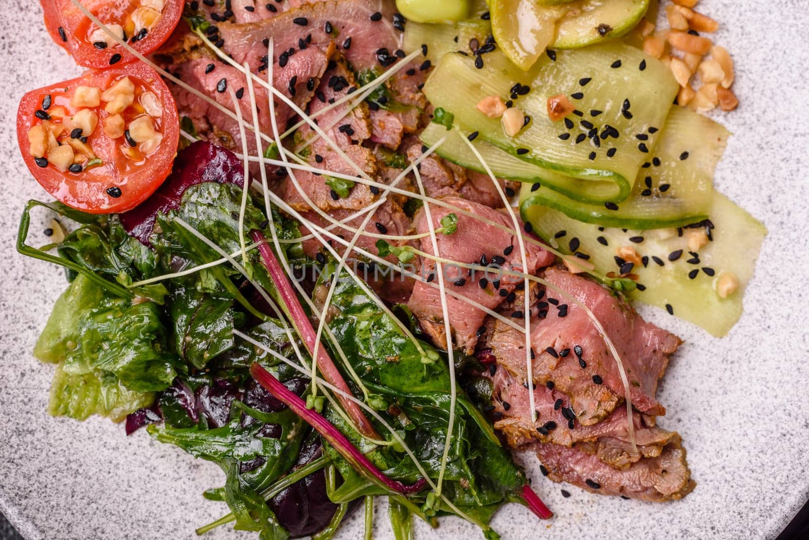 Warm salad consisting of slices of roast beef, greens, tomatoes, cucumbers, green beans on a dark concrete background