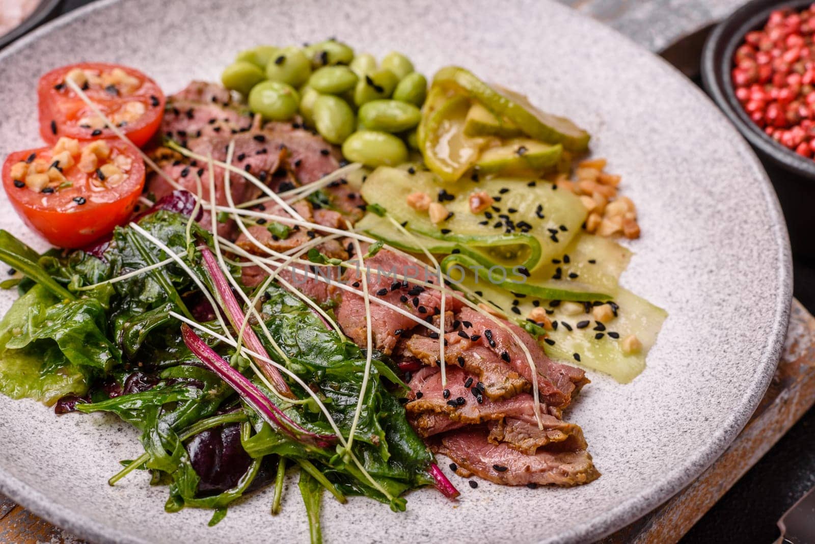 Warm salad consisting of slices of roast beef, greens, tomatoes, cucumbers, green beans on a dark concrete background