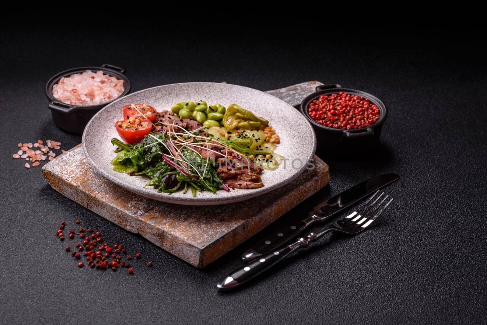 Warm salad consisting of slices of roast beef, greens, tomatoes, cucumbers, green beans on a dark concrete background