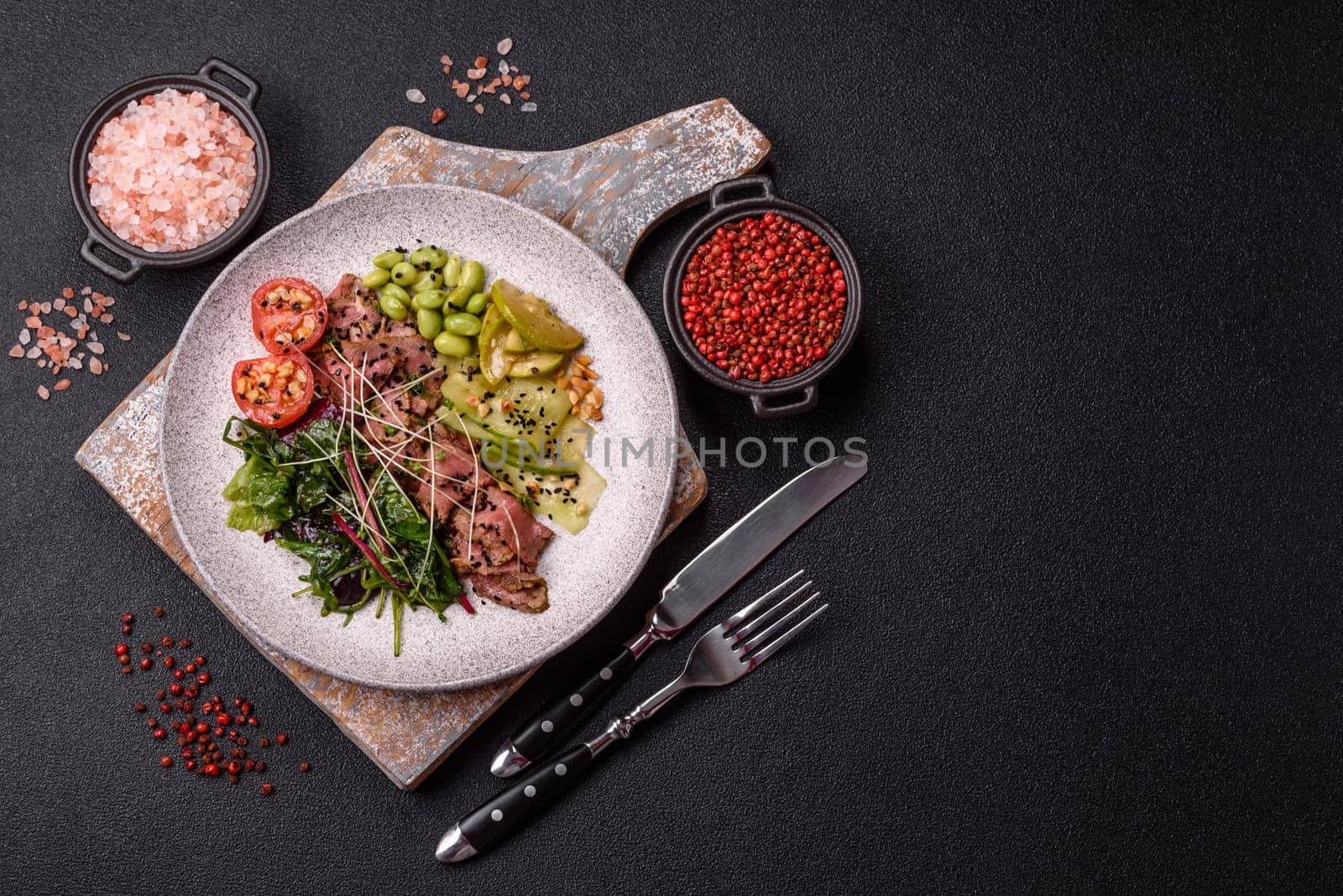 Warm salad consisting of slices of roast beef, greens, tomatoes, cucumbers, green beans on a dark concrete background