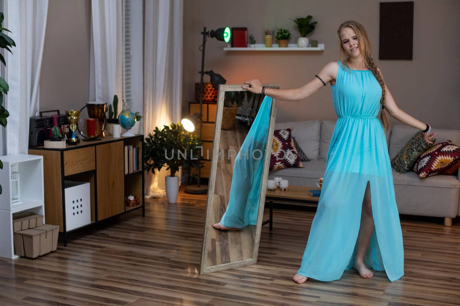 A stylish and fashionable woman dressed in a vibrant turquoise outfit is gracefully posing in a cozy living space