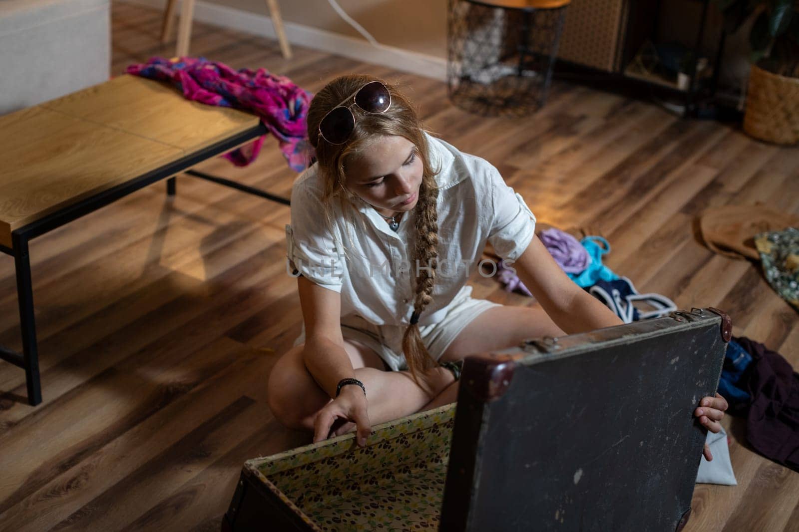 A young woman discovers nostalgic items in an antique trunk at home, surrounded by colorful fabrics.