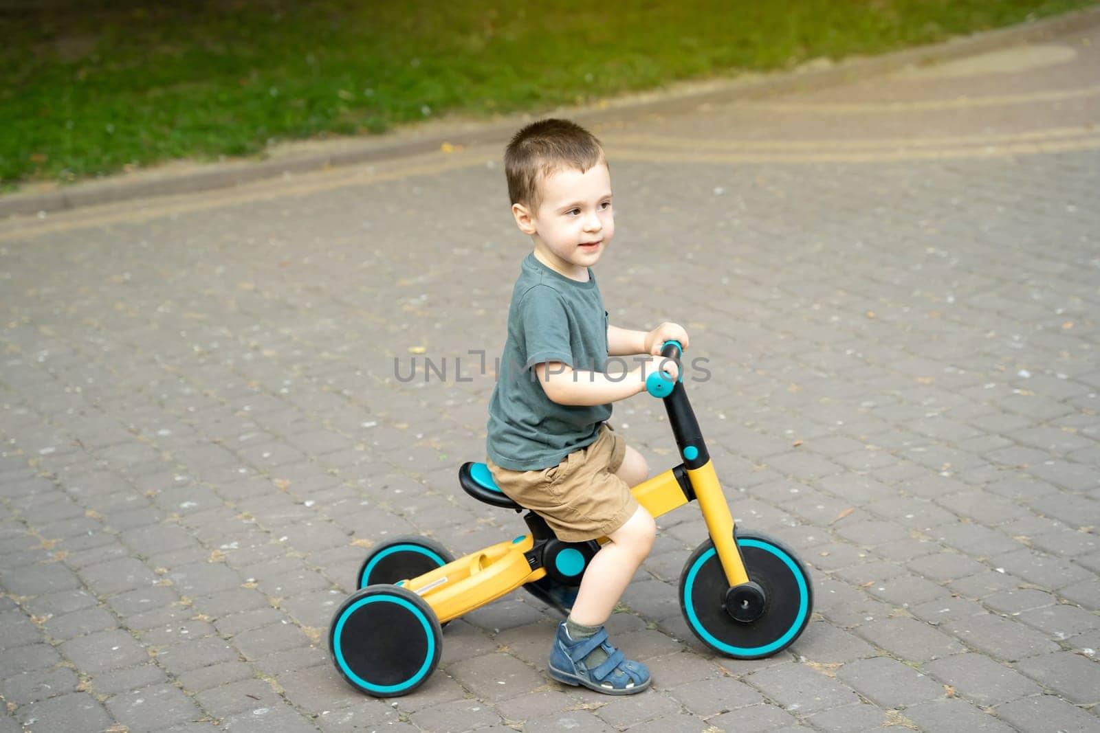 A cute toddler boy of two or three years old rides a bicycle or balance bike in a city park on a sunny summer day. Toddlerhood and childhood concept. Selective focus