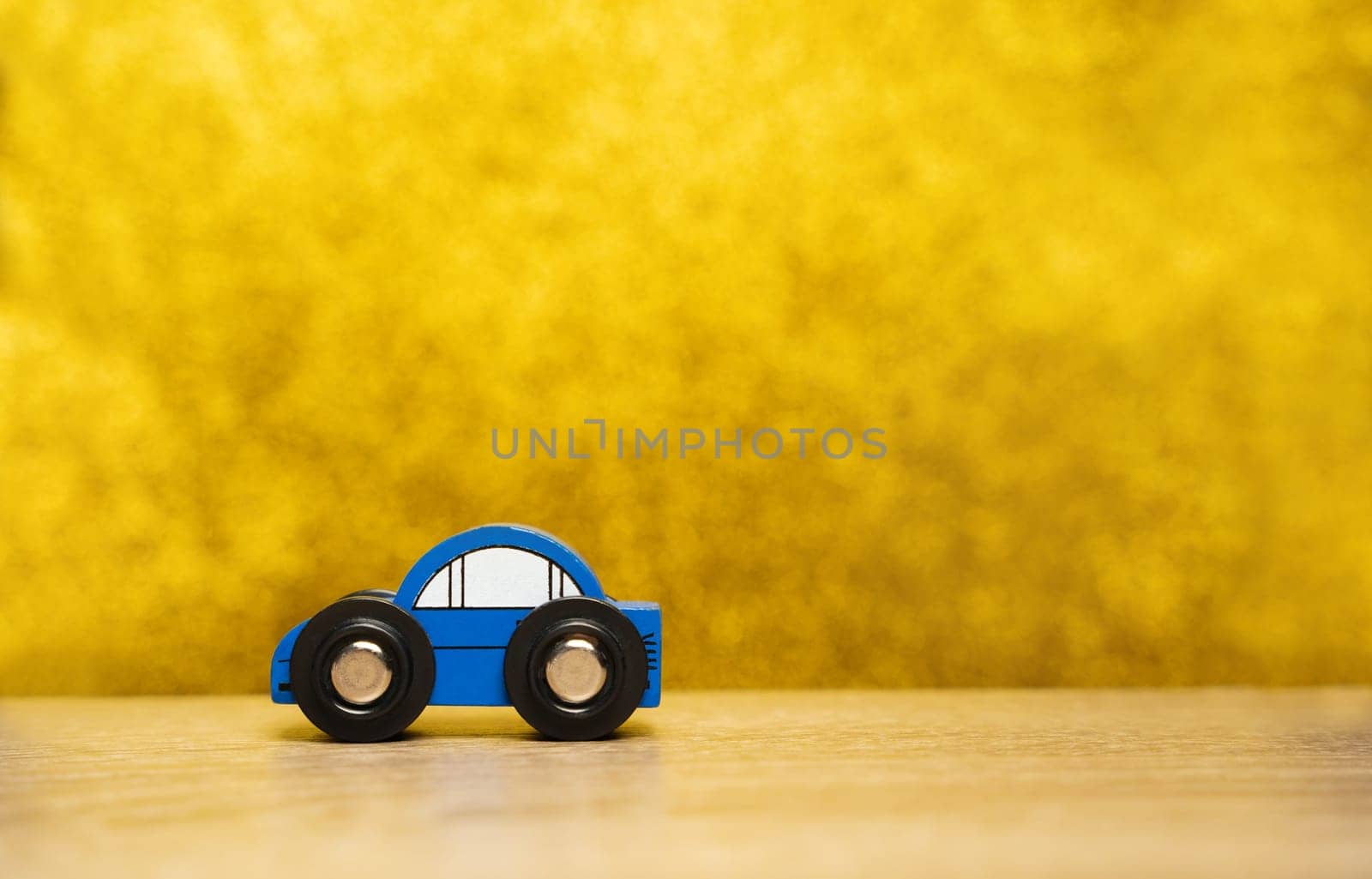 A small blue toy car on a yellow background. The concept of auto insurance, buying and selling cars. Repair and maintenance of vehicles. Copy space