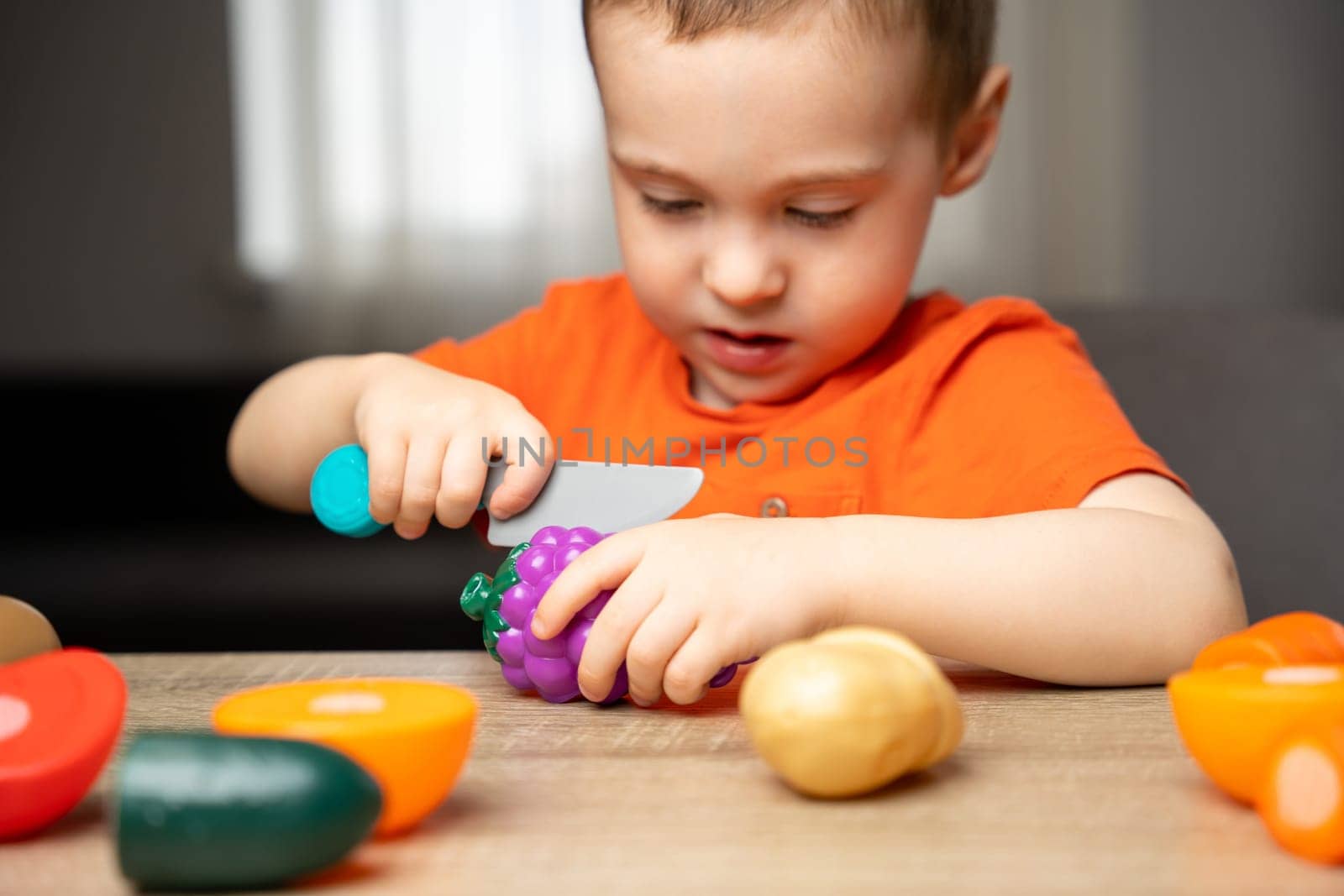A cute 3 year toddler boy plays with toy fruits or vegetables and sitting at the table. Velcro games. Selective focus