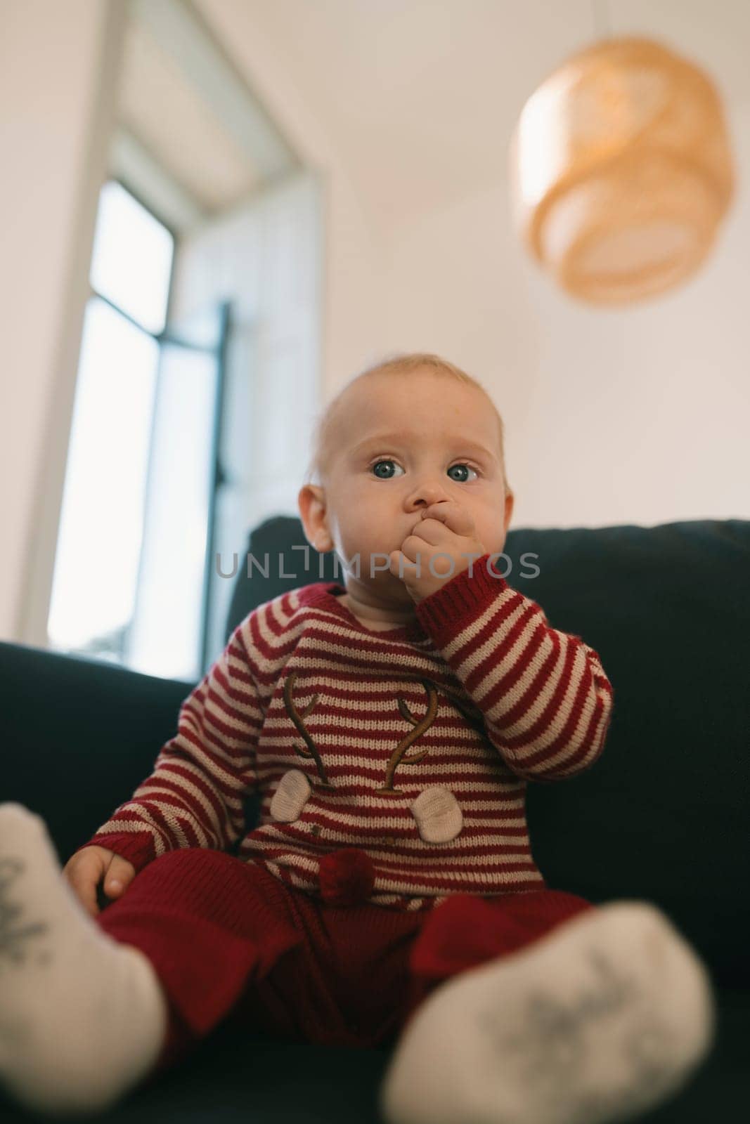 A charming and adorable baby wearing striped pajamas is sitting indoors with a sweet and playful expression