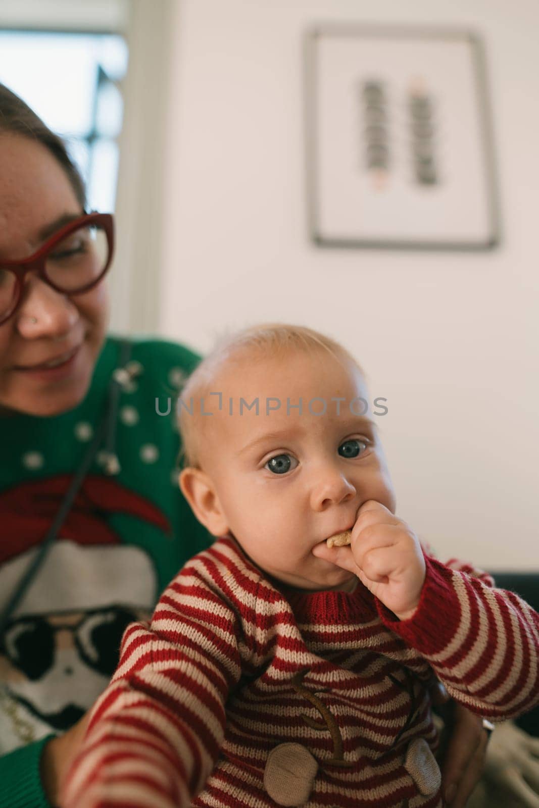 A cheerful baby dressed in striped pajamas happily eats a tasty snack while being lovingly held by a smiling parent