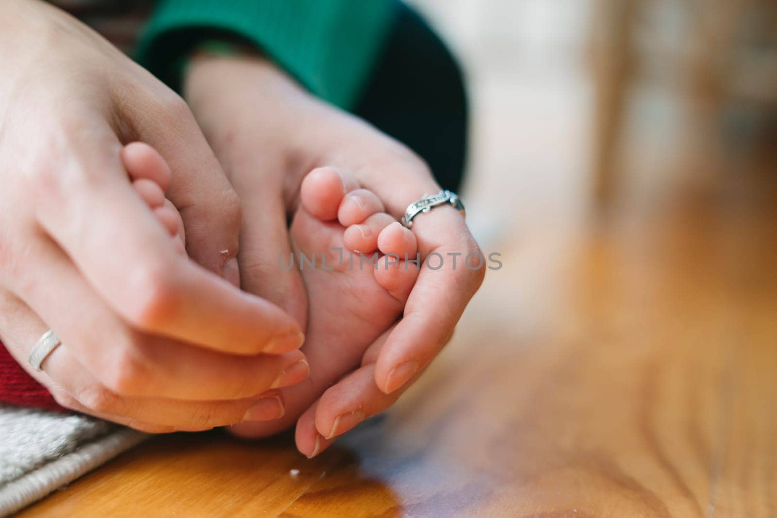 A beautifully heartfelt moment captured of hands gently cradling a babys tiny feet resting on a wooden floor